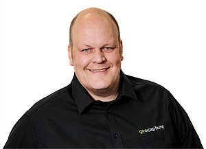Porträt eines lächelnden Mannes im schwarzen Hemd mit geoCapture-Logo vor weißem Hintergrund