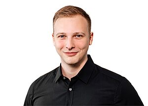 Porträtfoto eines lächelnden Mannes mit kurzem Haar, schwarzem Hemd und hellem Hintergrund