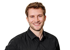 Porträt eines lächelnden Mannes in schwarzem Hemd vor weißem Hintergrund