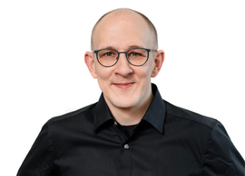 Porträt eines Mannes mit Brille im schwarzen Hemd vor weißem Hintergrund