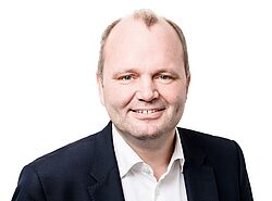 Porträt eines freundlich lächelnden Mannes im Business-Outfit vor weißem Hintergrund